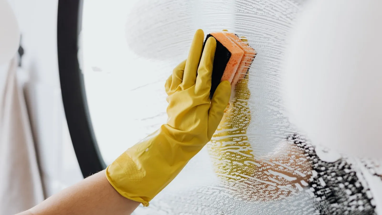 Close-up of streak-free mirror detailing with sponge during deep cleaning service